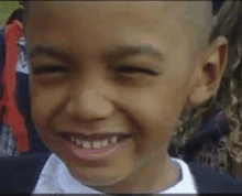 a young boy with a shaved head is smiling with his eyes closed .