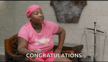 a woman in a pink shirt is sitting in a chair with congratulations written on the screen behind her