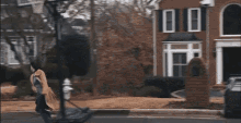 a woman is walking down a sidewalk in front of a house with a fire hydrant in front of it .