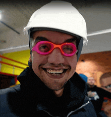 a man wearing a white hard hat and pink goggles smiles for the camera