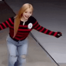 a woman wearing a red and black striped sweater and ripped jeans is dancing on a stage .