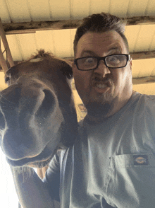 a man wearing glasses and a dickies shirt holds a horse