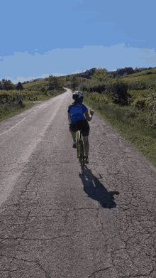 a person riding a bike down a road wearing a helmet and a blue shirt that says ' a ' on it