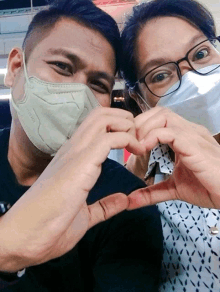 a man and a woman wearing face masks make a heart shape with their hands