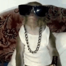 a monkey wearing sunglasses and a chain is sitting on a couch holding a bottle of beer .