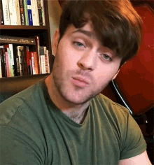 a man in a green shirt is looking at the camera in front of a bookshelf with a book titled tempest