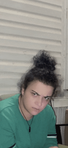 a woman with curly hair in a bun is wearing a green shirt