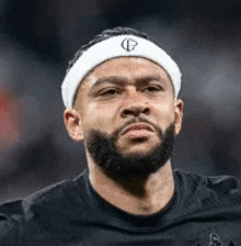 a man with a beard is wearing a headband and looking at the camera .