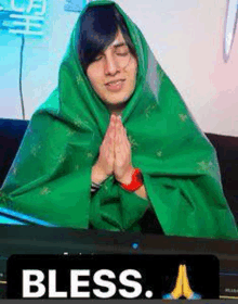 a man wrapped in a green blanket is praying in front of a computer screen .