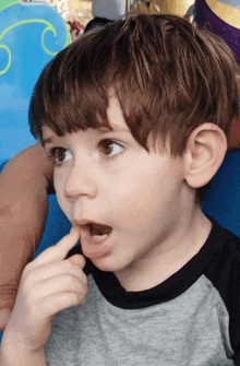 a young boy with a finger in his mouth looks at the camera