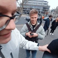 a man wearing glasses holds another man 's wrist while looking at his phone