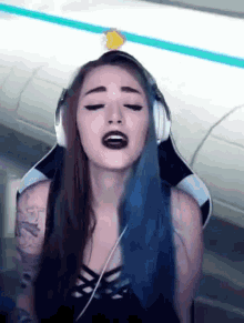 a woman with blue hair is wearing headphones and singing into a microphone while sitting in a chair .