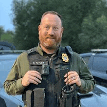 a man with a beard is standing in front of a car holding a walkie talkie .