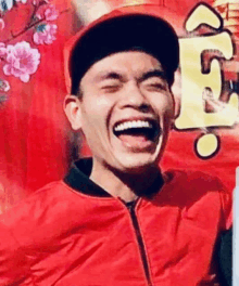 a man wearing a red jacket and a baseball cap is laughing .