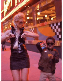 a woman in a black dress is dancing next to a little boy who is holding a bottle of soda