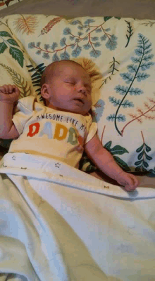 a baby wearing an awesome like my daddy shirt is sleeping on a bed