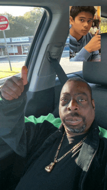 a man in a car giving a thumbs up next to a boy in front of a sign that says natural foods