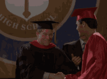 a man in a graduation cap and gown stands next to another man in front of a high school banner