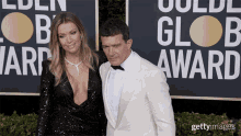 a man in a white suit and a woman in a black dress pose on the red carpet at the golden globes