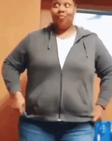 a woman is wearing a gray hoodie and jeans and making a funny face .