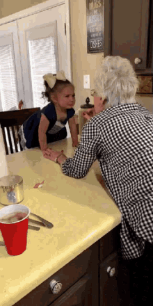 a little girl is sitting at a kitchen counter with an older woman and a sign that says hugs are miracles