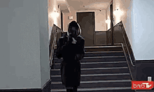 a woman is walking down a set of stairs in a hallway .