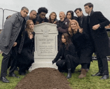 a group of people posing for a picture in front of a gravestone that says " ouvier queen "