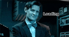 a man in a suit and bow tie is sitting in a dark room with the words `` loading '' above him .