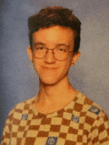 a young man wearing glasses and a checkered shirt looks at the camera