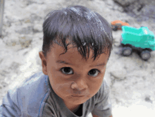 a little boy with a green truck in the background looks at the camera