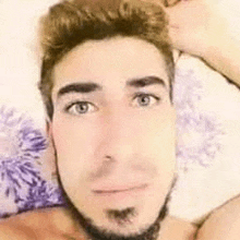 a shirtless man with a beard is laying on a bed and making a funny face .