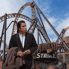 a man in a suit is standing in front of a roller coaster and a sign that says " strike "