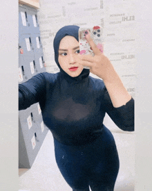 a woman wearing a hijab takes a selfie in front of a wall that says ' othorot ' on it