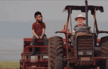 a man is sitting on the back of a tractor while another man is driving it .