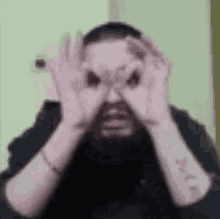 a man with a beard is making a funny face with his hands in front of his eyes .