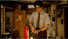 a man in a plaid shirt and tie is standing in front of a fire extinguisher