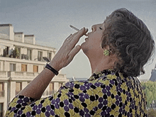 a woman in a yellow and purple polka dot shirt smoking a cigarette