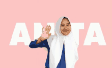 a girl wearing a hijab and a white scarf is waving in front of the word anta