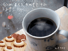 a cup of coffee sits on a table next to cupcakes with hearts on them