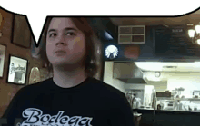 a man wearing a black bodega shirt stands in a kitchen