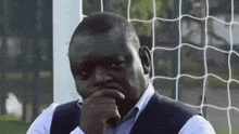 a man is sitting in front of a soccer net with his hand to his chin .