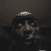 a man wearing a hat and a bandana is smoking a cigarette in a dark room .