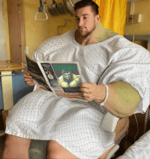 a man in a hospital gown is reading a newspaper with a picture of the hulk on the front