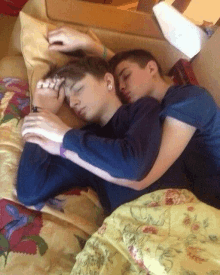 two young men are sleeping in a bed together .