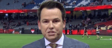 a man in a suit and tie is talking on a soccer field .