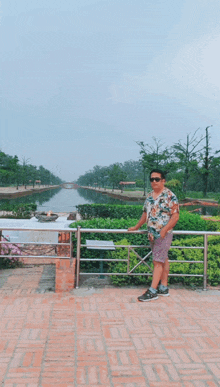 a man is standing on a brick walkway next to a fence with a river in the background