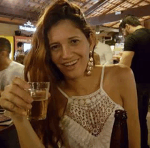 a woman is holding a glass of beer and smiling while sitting at a table .