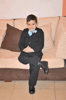 a young boy in a suit and tie sits on a couch