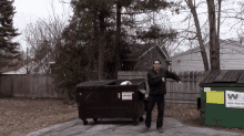 a man stands in front of a dumpster that has a sticker on it that says ' recycling ' on it