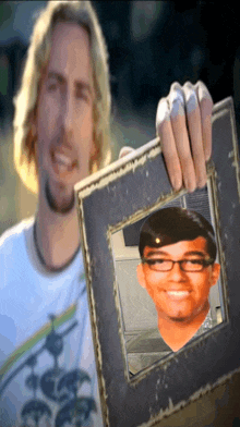 a man is holding a picture frame with a picture of a young man with glasses on it